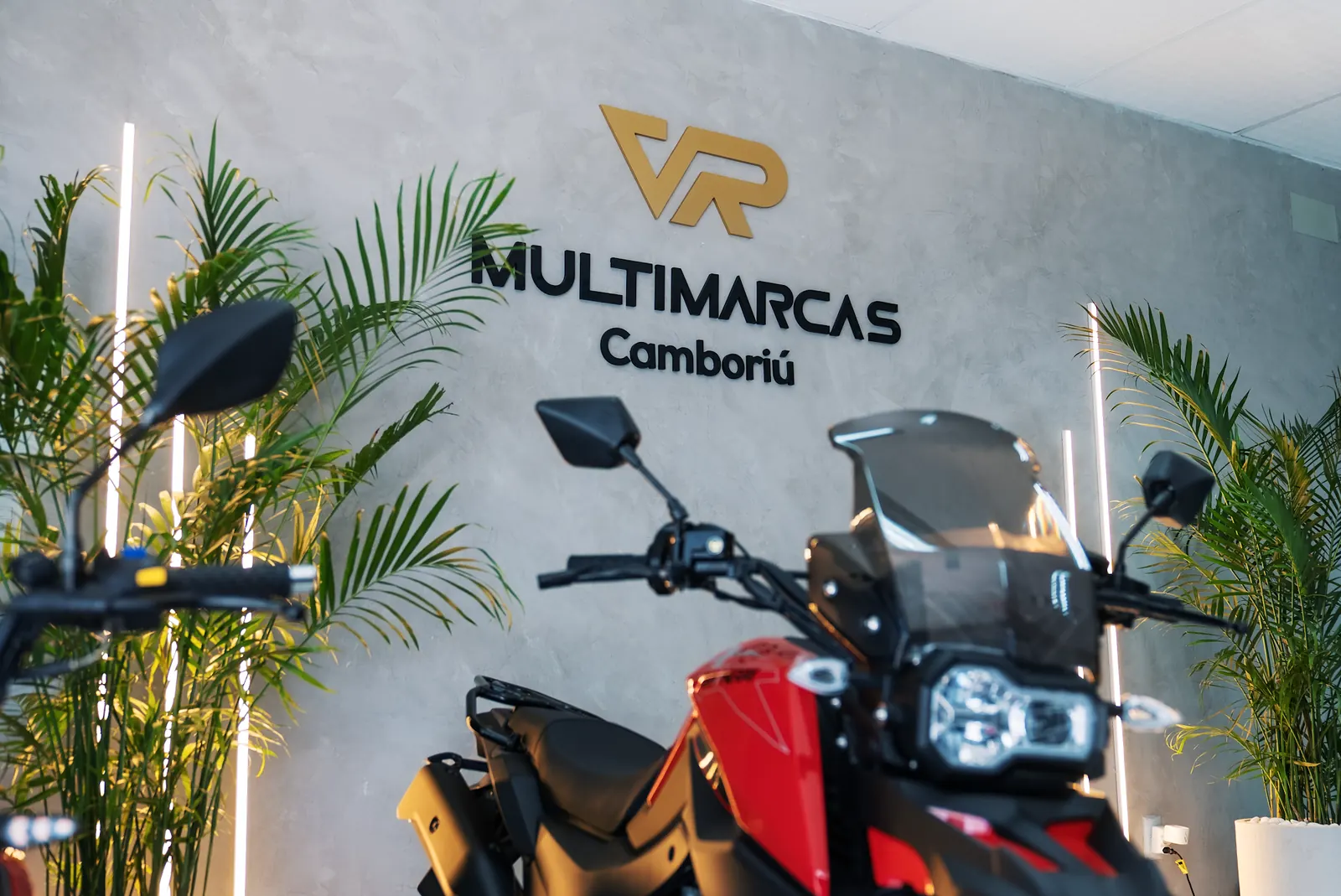 Showroom da VR Multimarcas Camboriú com moto na frente do logo e plantas